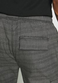 Grå rutiga byxor med en bakficka, strukturerad tyg och en avslappnad passformdesign med subtila linjer och mönster.
