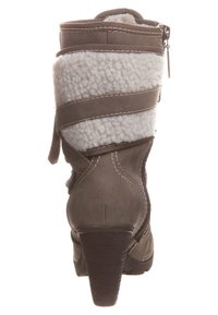 Brązowe skórzane botki za kostkę z kapturem z sztucznego futra i krzyżującymi się paskami. Lekko spiczasty nosek i teksturowany obcas. Zamek błyskawiczny po boku.