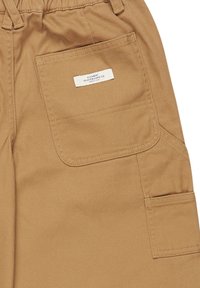 Beige Cargo-Hosen aus strapazierfähigem Stoff mit mehreren Taschen, einem elastischen Bund und einem kleinen Markenlabel, das auf die Gesäßtasche genäht ist.