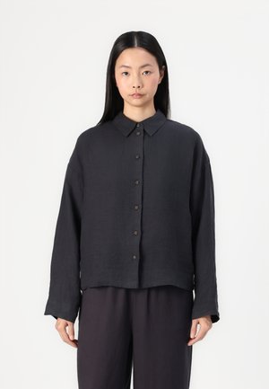 Chemise à manches longues noire grise, en lin. Présente un col pointu, des boutons à l'avant et une coupe décontractée avec une longueur légèrement raccourcie.