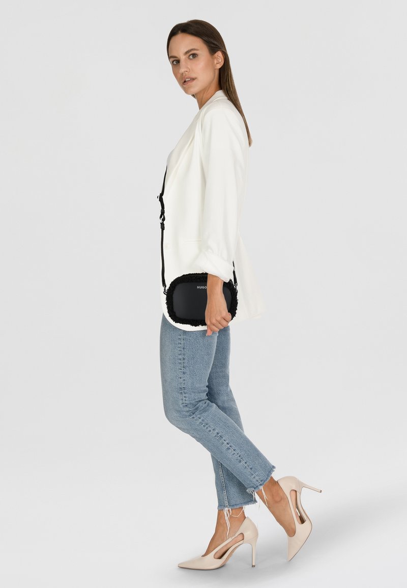 Blazer bianco con bordi neri, borsa nera con dettagli in pelliccia, jeans skinny azzurri e scarpe con tacco beige.