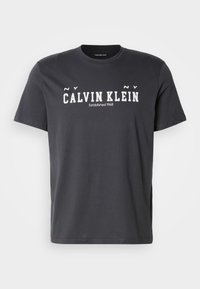 Must musta T-särk, millel on ümmargune kaelus, lühikesed varrukad ja julge valge kiri "CALVIN KLEIN Established 1968" ees.