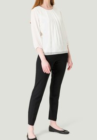Blouse blanche plissée à manches trois-quarts, assortie à un pantalon noir ajusté et des ballerines noires. Tissu lisse, design simple.