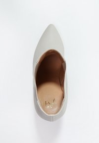 Grijze puntige schoen met een gladlederen bovenwerk, open zijden en een tankleurige binnenzool met gouden branding. Platte zool, minimalistisch ontwerp.