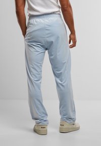 Pantaloni da jogging in morbido tessuto azzurro chiaro con vita elasticizzata. Presentano una vestibilità comoda e si stringono alla caviglia. Sneakers bianche visibili.