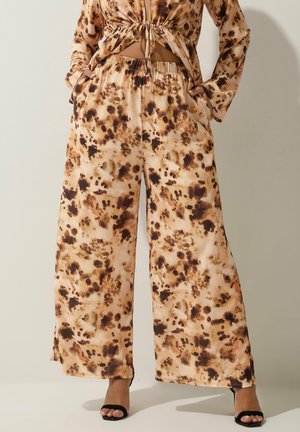 Pantalones de pierna ancha hechos de una tela suave con un patrón de teñido anudado en marrón y beige. Cintura elástica con bolsillos laterales, combinados con tacones negros.