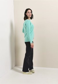 Mintgrön ribbad tröja, svarta vida byxor och ljusa sneakers. Modellen står på sidan mot en neutral bakgrund.