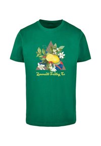 Žalias medvilninis marškinėliai su trikampiu grafiniu piešiniu, kuriame yra citrinos, lapai ir gėlės, o apačioje užrašyta "Lemonade Trading Co."