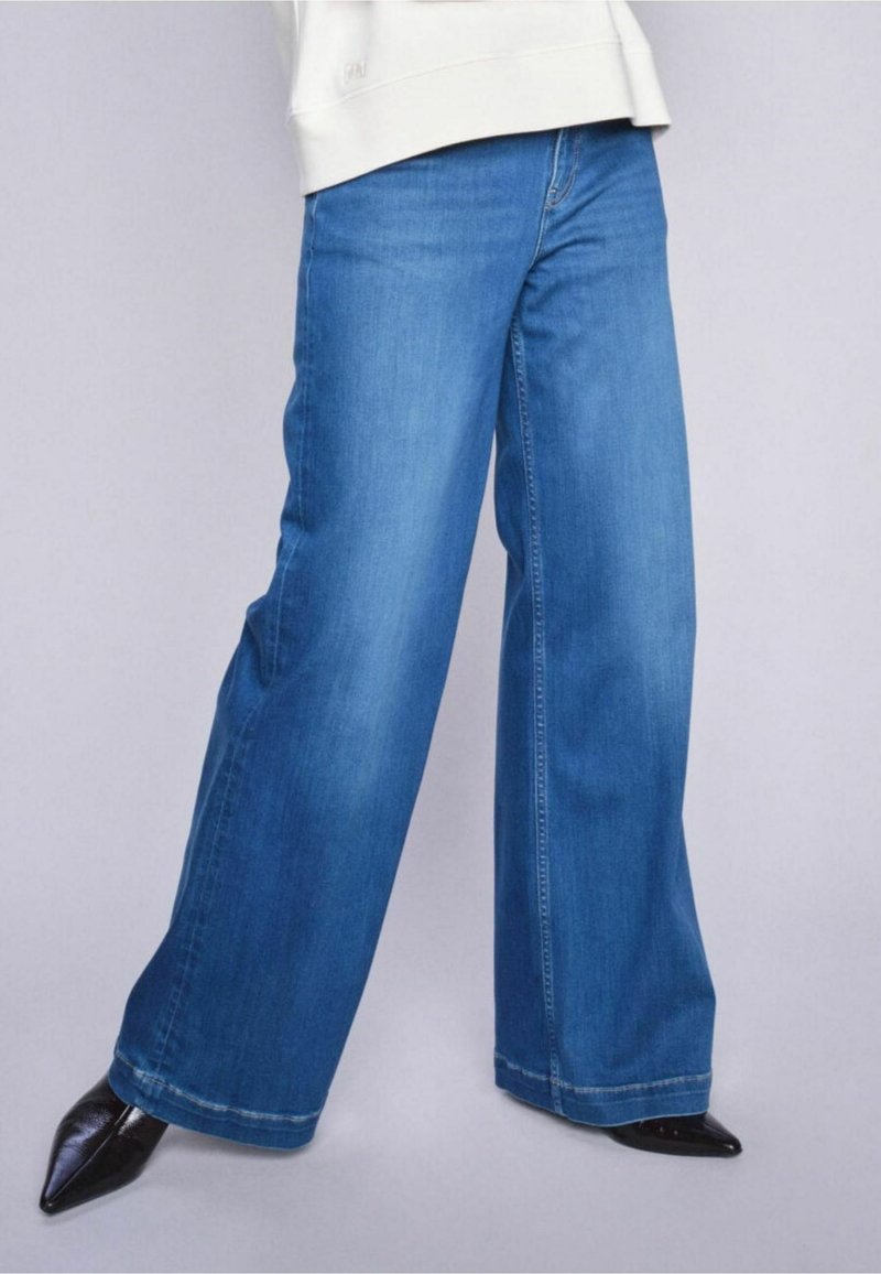 Wijdvallende blauwe denim jeans met een lichte wassing, voorzien van een rechte snit en zichtbare stiksels. Gecombineerd met puntige zwarte hakken.