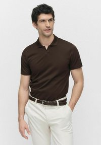 Bruine polo shirt van zachte stof, met een kraag en korte mouwen, gecombineerd met witte broeken en een gevlochten bruine riem.