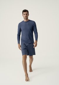 Marinblå langærmet sports T-shirt parret med matchende shorts. Stoffet fremstår glat med en let og åndbar tekstur. Minimalistisk design, uden mønstre.
