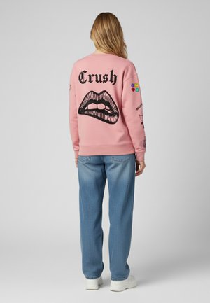 Felpa di cotone rosa con una grande grafica di labbra nere e la parola "Crush" sul retro, completata da toppe colorate sulle maniche.