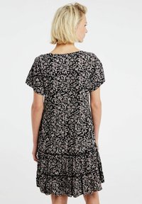 Schwarzes Kleid mit floralem Muster in Rosa und Weiß. Kurze Ärmel, runder Ausschnitt und mehrlagiger Rüschensaum mit lockerer Passform.
