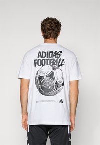 Hvid bomuld t-shirt med et stort sort grafisk motiv af en fodbold og "ADIDAS FOOTBALL" tekst på ryggen, med logo accenter.