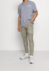Ljusgrå t-shirt med logotyp, kombinerad med olivgröna cargobyxor med sömdetaljer och sidofickor, kompletterad med vita sneakers.