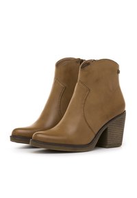 Par de botas de tobillo de cuero beige con tacones de bloque apilados y cremalleras laterales sobre un fondo blanco.