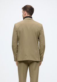 Beige op maat gemaakt pak met een geknipt kraag, enkele split en knoopmanchetten. Gladde textuur, slank ontwerp met minimalistische details.