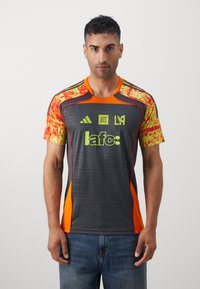 Grå atletisk trøje med orange og gule detaljer. Har et grafisk mønster, rund halsudskæring, og logoer på fronten. Kortærmet design.