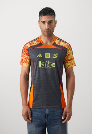 Grijze sporttrui met oranje en gele accenten. Heeft een grafisch patroon, ronde halslijn en logo's aan de voorkant. Korte mouwen.