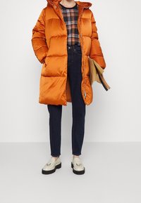 Orange puffjacka med huva, vadderad design, glansig finish. Tillsammans med mörka denimjeans och krämfärgade loafers med svarta sulor.