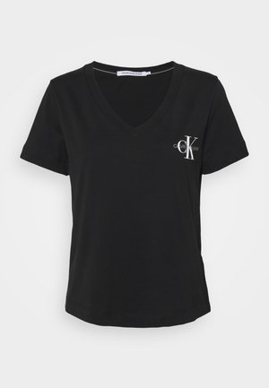 T-shirt nera a maniche corte con scollo a V e logo bianco di Calvin Klein Jeans sul lato sinistro del petto, esposto su uno sfondo bianco semplice.