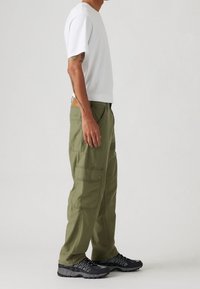 Witte katoenen ronde hals T-shirt, gecombineerd met olijfgroene cargobroek met zijzakken, afgewerkt met zwarte sportschoenen met een gestructureerde zool.