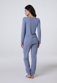 Set di pigiama blu a coste con maniche lunghe e pantaloni affusolati. Tessuto morbido, caratterizzato da una scollatura ampia e polsini arricciati sui pantaloni.