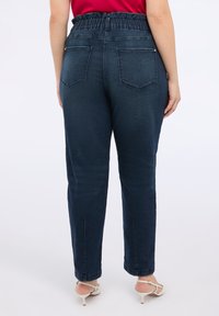 Dunkelblaue Jeanshose mit einem gerafften Elastikbund, geradem Bein-Design und zwei hinteren Taschen. Glatte Textur und eng anliegende Knöchel.