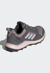 Zapato de senderismo gris y lavanda con parte superior de malla y sintético, tres franjas blancas, cuello acolchado y suela de goma texturizada.
