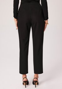 Dopasowane czarne spodnie o gładkiej fakturze, prostym kroju nogawek i dyskretnych kieszeniach z tyłu. Połączone z czarnymi sandałami na wysokim obcasie z odkrytymi palcami.