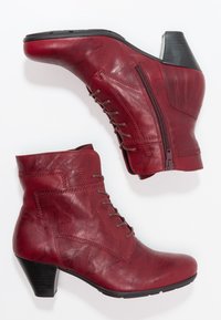 Botas de tobillo de piel roja con un diseño elegante, que cuentan con una cremallera lateral, cierre de cordones en la parte frontal y un tacón apilado. Textura suave con costuras detalladas.