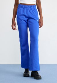 Blue athletic pants with a wide leg, elastic waistband, and contrasting white stripe; made from smooth, lightweight fabric.
