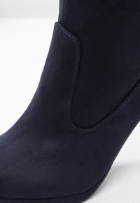 Gros plan sur une botte cheville en cuir suédé bleu foncé avec bout arrondi et couture décorative sur le côté.