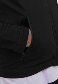 Schwarze Zip-Jacke mit einer Fronttasche und strukturiertem Stoff. Der Bund ist enganliegend, und der untere Saum hat einen sauberen Abschluss.