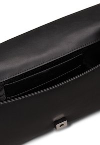 Clutch bag in pelle nera con una texture liscia, forma rettangolare e chiusura a scatto metallica. L'interno include uno scomparto per carte.