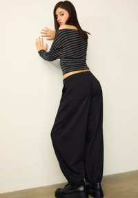 Pruhovaný čierny a šedý skrátený top a voľné čierne nohavice. Ploche čierne topánky s hrubou podrážkou. Model pózuje proti stene.