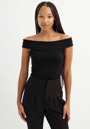 Top negro de hombros descubiertos con un diseño ajustado, confeccionado en una tela suave. Combinado con pantalones negros de cintura alta con pliegues.