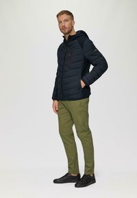 Marineblauwe gewatteerde jas met een capuchon, ritszak op de borst in het rood, elastische manchetten; gecombineerd met olijfgroene broek en zwarte sneakers.