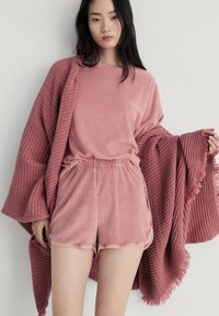 Rosa loungeoutfit bestående av en mjuk, strukturerad omlottjacka och matchande topp och shorts, allt i ett bekvämt, plyschigt tyg med en avslappnad passform.