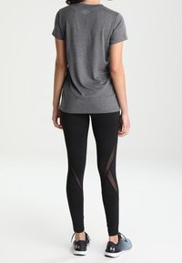 Graues kurzärmliges Sportshirt, kombiniert mit schwarzen Leggings mit transparenten Seiteneinsätzen. Schuhwerk: dunkle Sneakers. Schlichtes, funktionales Design.