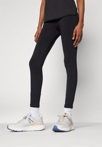 Sorte atletiske tights med et fitted design, parret med lysegrå joggesko med blå og oransje detaljer. Teksturert stoff.