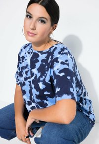 Modrá tie-dye oversized tílko s krátkým rukávem, s tmavě modrými a světle modrými víry, spárované s tmavými džíny.