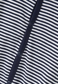 Randig bomullstyg i marinblått och vitt, med en knappslå med mörka, runda knappar längs mitten, mjuk textur och avslappnad design.