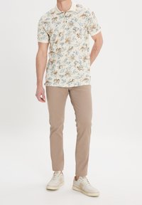 Pohodová polokošile s krátkým rukávem v krémové barvě, zdobená modrými a béžovými květinami, s světle béžovými chinos kalhotami a bílými teniskami. Jednoduchý design límečku.