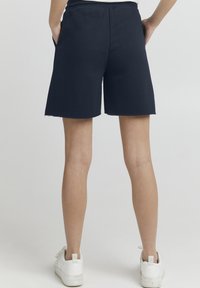 Marineblå bomuldsshorts med en afslappet pasform, længde til midt på låret, frynset kant og sidelommer. Båret med hvide sneakers.