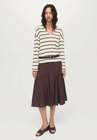 Gestreiftes langärmliges Shirt in Creme und Dunkelbraun, kombiniert mit einem braunen Glockenrock. Schwarze Sandalen vervollständigen das Outfit, das eine taillierte Taille aufweist.