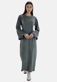 Vestito grigio a maniche lunghe con vestibilità ampia, scollo tondo e maniche svasate. Indossato con sneakers bianche e tessuto a trama.