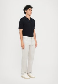Marineblauw poloshirt met een kraag, gecombineerd met lichtbeige broek. Model staat rechtop en draagt crèmekleurige sneakers. Eenvoudig, strak ontwerp.
