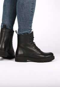 Stivaletti neri in pelle con una finitura testurizzata, lacci frontali e suola in gomma resistente. Presentano una cerniera laterale e un'etichetta sul retro.