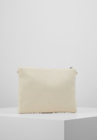Pochette en toile beige avec une texture lisse, forme rectangulaire, fermeture éclair supérieure et design minimaliste. Aucun motif ou accent visible.